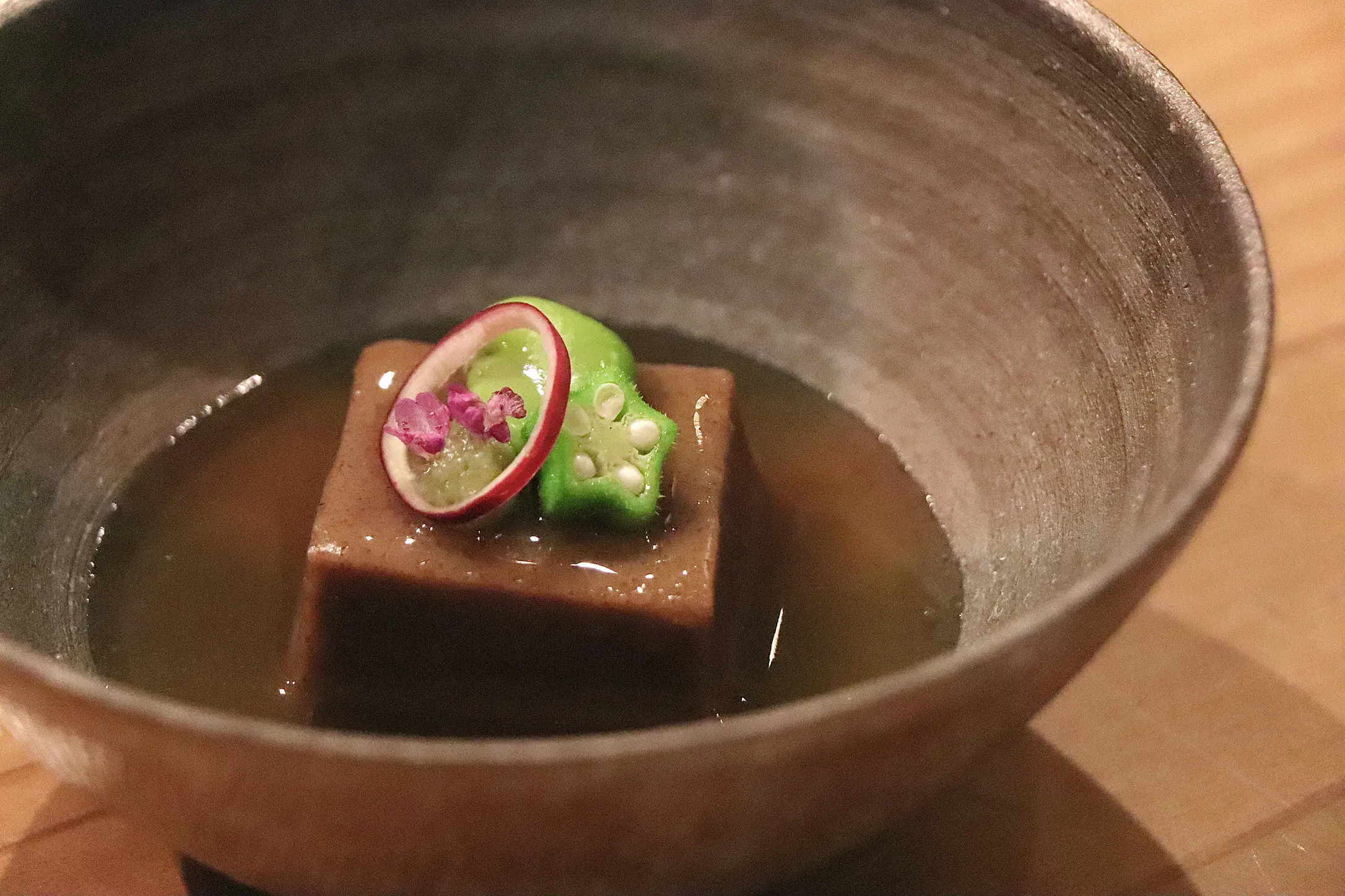 麦こがし豆腐の葛餡掛け。香ばしい麦こがしの風味を閉じ込めた自家製豆腐に、とろみのある葛餡をかけ、彩りとしてオクラ、赤かぶ、花穂紫蘇をあしらった一品。